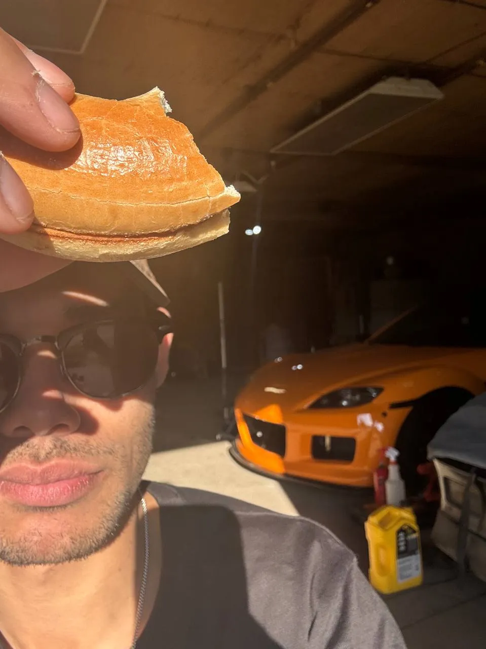 Noah Morris in his garage holding a sandwich, with his orange Mazda RX-8 behind him